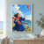 A smiling woman in a blue coat holds a kite string on a coastal headland as a red kite flies overhead, with gulls and ocean beyond.; frame shown for styling only