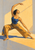 Adult dancer in a blue top and ochre wide-legged trousers holding a low side lunge in a sunlit room.