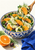 A patterned blue-and-white bowl of citrus, shaved fennel, greens, and olives, with a spoon lifting a bite and a cut orange beside it.
