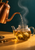 Copper gooseneck kettle pouring amber tea into a glass teapot with pale blossoms, with a tea bowl on a saffron surface.