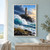 Stone lighthouse with an amber-lit window above a rugged black-rock headland and a large curling wave.; frame shown for styling only