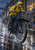 Cyclist in a bright yellow rain jacket riding a dark bicycle with a front basket through a rainy lane beside brick workshop windows.