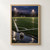 Football resting in a reflective puddle on a dark, rain-wet pitch at dusk, with white field lines, a distant goal, and floodlights.; frame shown for styling only