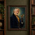 Elderly mustached inventor in a dark blue coat and gold scarf presenting an open-winged brass mechanical bird against teal.; frame shown for styling only