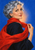 Fashion illustration of a woman with short silver-blue curls holding a flowing red scarf against a cobalt-blue background.