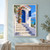 A whitewashed coastal house with a cobalt arched doorway, open blue shutter, flowering vine, terracotta pot, stone steps, and turquoise sea beyond.; frame shown for styling only