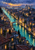 Elevated view down a turquoise canal through a dense city of terracotta rooftops, lit windows, an arched bridge, and distant hills at sunset.