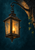 Illuminated iron lantern with a small flame, hanging from a bracket on a dark stone arch with ivy.