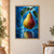 Golden-green and burgundy pear hanging beneath water-beaded green leaves, with a large droplet and bright blue background.; frame shown for styling only