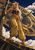 Horned barefoot woman holding a long dark staff before a huge gold-and-blue astronomical clock under a clouded sky.