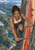 Pointed-eared woman climbing a fixed metal ladder on a sheer cliff, with a green mountain valley to the left and a glowing orange-red feature to the right.