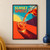 A clear carafe pours blood-orange soda into a tumbler with an orange slice against angular turquoise, yellow, orange, and plum shapes; “SUNSET SPRITZ” appears at upper left.; frame shown for styling only