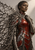 Dark-skinned woman with short textured hair in red and gunmetal armor, with thorn-like metal branches radiating from her shoulders.