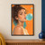 Close portrait of a woman with dark wind-swept curls blowing a large translucent turquoise bubble against an orange background with teal accents.; frame shown for styling only
