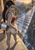 Pointed-eared woman with long dark braids holding a spool as luminous threads form a bridge across a gorge toward a distant city.