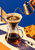 A hand pours water from a metal kettle into a glass pour-over coffee brewer beside a saffron cloth and two coffee beans.