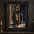 Woman in a green and gold gown standing beside an ornate framed shadowy portrait in a dim gallery.; frame shown for styling only