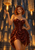 Red-haired woman in a glossy dark red dress with a floating flame above her hand in a shadowy Gothic interior.
