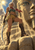 An anime-styled woman with pale braids and a curved sword stands on a stone ledge among golden desert ruins, with a giant carved face behind her.