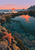 An orange sea star rests on a rocky edge beside a deep teal tidepool reflecting a coral sunset, with a distant headland.