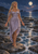 Barefoot woman with long pale braids and a flowing lavender dress standing on coastal rocks beneath a full moon, with foaming water.
