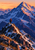 Two mountaineers on a rocky snow-streaked ridge beneath a large blue alpine peak at sunset; the nearer climber wears red-orange.