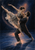 Two adult contemporary dancers in a supported lift, with one reaching outward and extending a leg behind on a dark stage.