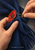 Hands fastening a red enamel flower-shaped brooch over a folded navy scarf, with the open pin visible.