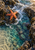 An orange-red five-armed sea star clings to wet rock beside white foam and clear teal tidepool water.