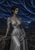 Pointed-eared dark elf in a silver pleated gown seated on a rocky ledge above a valley beneath a layered blue night sky.