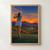 Woman golfer seen from behind with her club across her shoulders, overlooking a desert golf course at sunset.; frame shown for styling only
