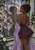 Dark-haired woman in plum and lavender beside an arched mirror showing patterned moth-like wings in the reflection.