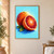 Whole orange behind an upright halved blood orange, showing crimson radial flesh, with two green leaves against a pale aqua background.; frame shown for styling only