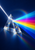 A triangular glass prism splits a white beam into vivid colored rays against a dark blue background.