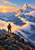 A lone hiker with a trekking pole stands on a rocky ridge facing a snowy mountain peak above sunrise-lit clouds.