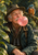 Elderly man in a dark outdoor hat and coat blowing a pink bubble, with binoculars at his chest and a blue-and-orange kingfisher on a leafy branch.