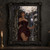 Dark-haired woman in a burgundy gown holding an oversized pale flower beneath a moonlit Gothic arch.; frame shown for styling only
