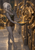 White-haired fantasy woman holds a bowl beneath a circular bronze mechanism pouring glowing liquid in a treasure-filled stone chamber.