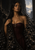 Dark-haired woman in a burgundy corset framed by glossy black strands beneath a crescent moon, with a distant city and mountains.