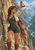 Woman in a rust-red headscarf and teal outfit raises a handbell on a rocky mountain path above a deep valley.