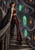Dark-haired woman in a black cape on twisting stone stairs beneath green-lit Gothic arches.