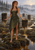 A barefoot auburn-braided woman in an olive dress stands in a misty bog among tall peat-like columns at sunrise.