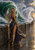 A woman in a flowing dark gown stands on a wet harbor wall before huge waves, with a lighthouse in the distance.