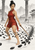 Barefoot swordswoman in a red wrap outfit stands with a sword among curved dark stones in a pale courtyard.