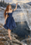 Red-haired woman in a blue dress raises a pale translucent sheet beside a snowy, partly frozen pond.