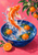 A bright orange koi twists above a cobalt bowl with mandarins, green leaves, white blossoms, and splashing water against a pink ground.