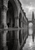 Monochrome stone arches and carved columns reflected in a pool, with a distant cypress beneath an overcast sky.