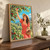 A woman in a coral dress and straw hat reaches toward cherries in an orchard while holding a basket, with hills and water in the distance.; frame shown for styling only