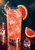 Illustrated pink grapefruit soda in a tall glass with ice and bubbles, grapefruit at the rim, a loose wedge and ice cubes, and a splash against a deep teal background.