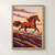 Illustrated chestnut horse leaping above a rugged ridge beneath a peach dawn sky and turquoise sun.; frame shown for styling only